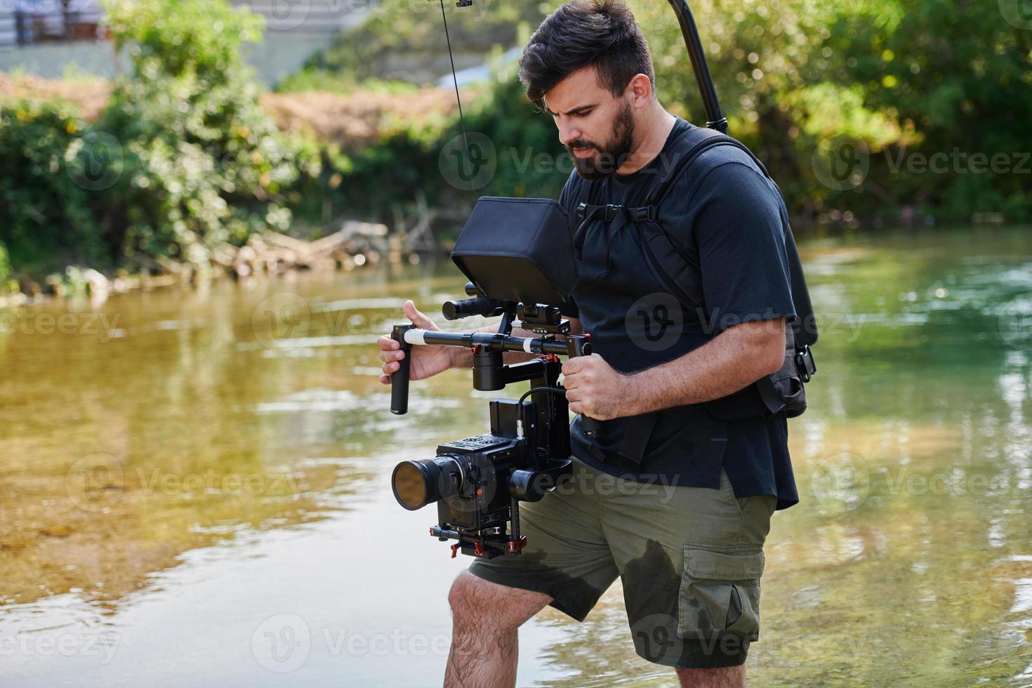 a professionally equipped cameraman shoots in the water surrounded by beautiful nature. photo