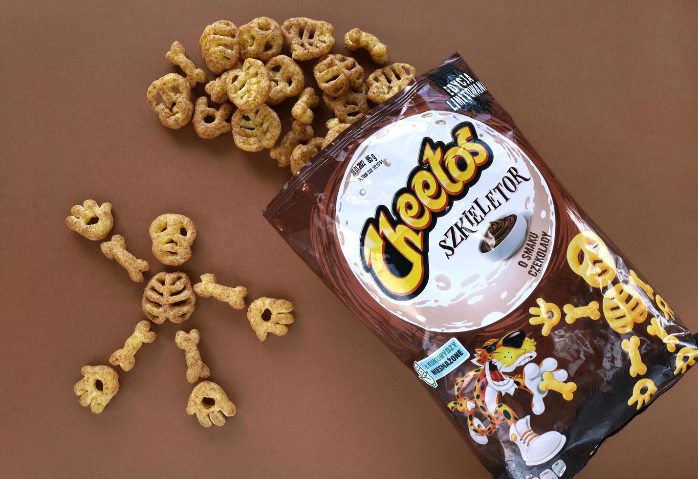 Krakow, Poland, 2021 - Bag of spilled puffed corn snacks Cheetos Skeleton with chocolate flavor on brown background. Skeleton parts - skull, rib cage, hands, feet, bones. Halloween treats. photo