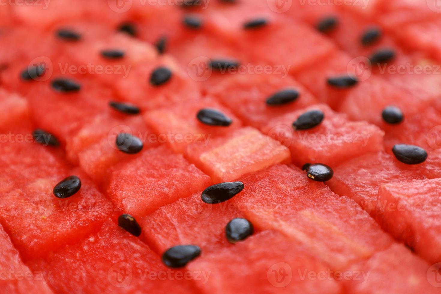 sandía madura roja cortada en cubitos en filas, las semillas negras están esparcidas en la parte superior. Jugosas piezas de fruta fresca sin costuras patrón geométrico de fondo. vista de perspectiva. lugar para el texto. foto