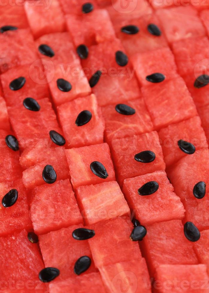 sandía madura roja cortada en cubitos en filas, las semillas negras están esparcidas en la parte superior. Jugosas piezas de fruta fresca dispuestas en un patrón geométrico de fondo vertical sin fisuras. lugar para su texto. foto