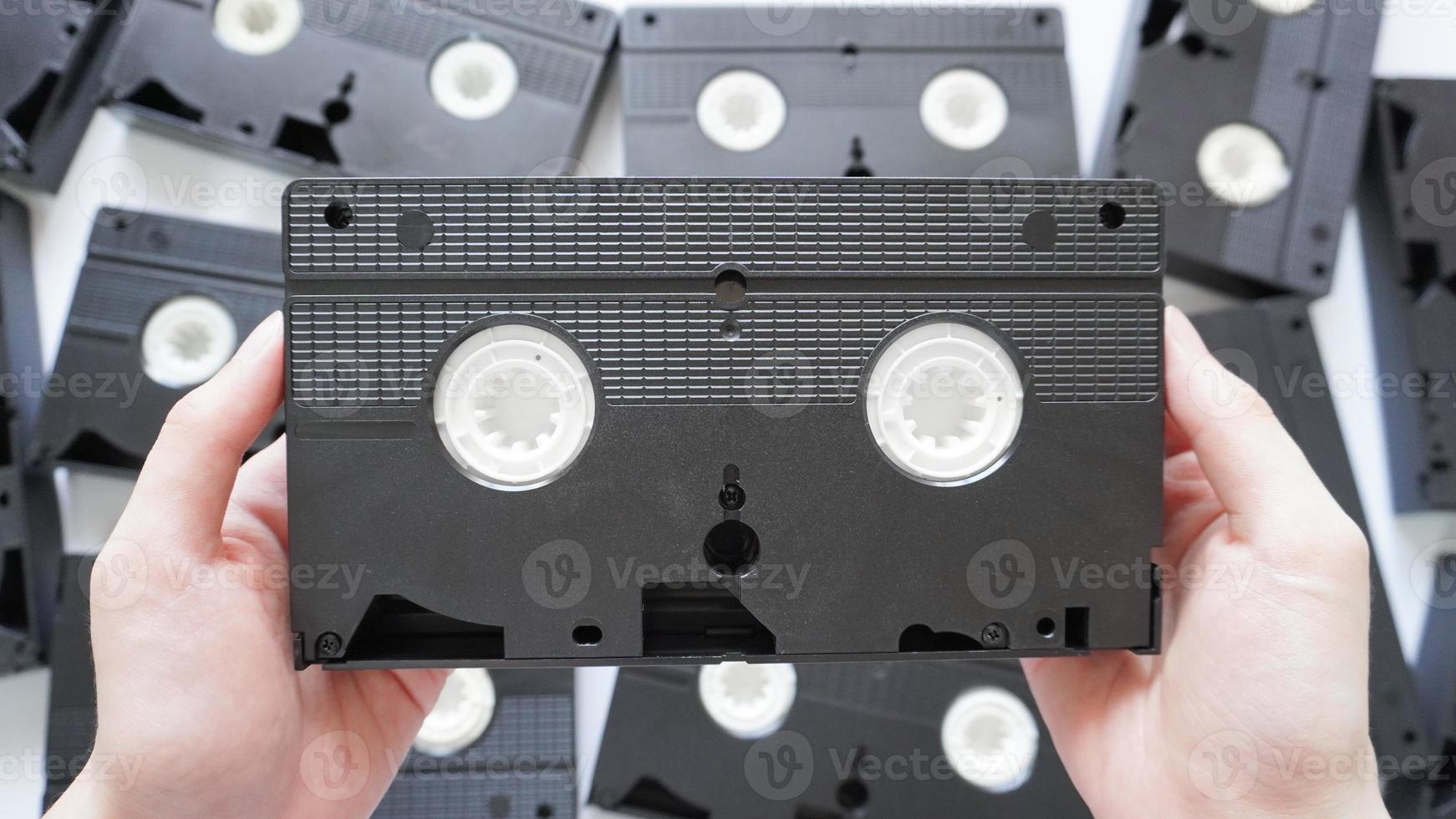 Hands holding a VHS tape back side with scattered tapes in the