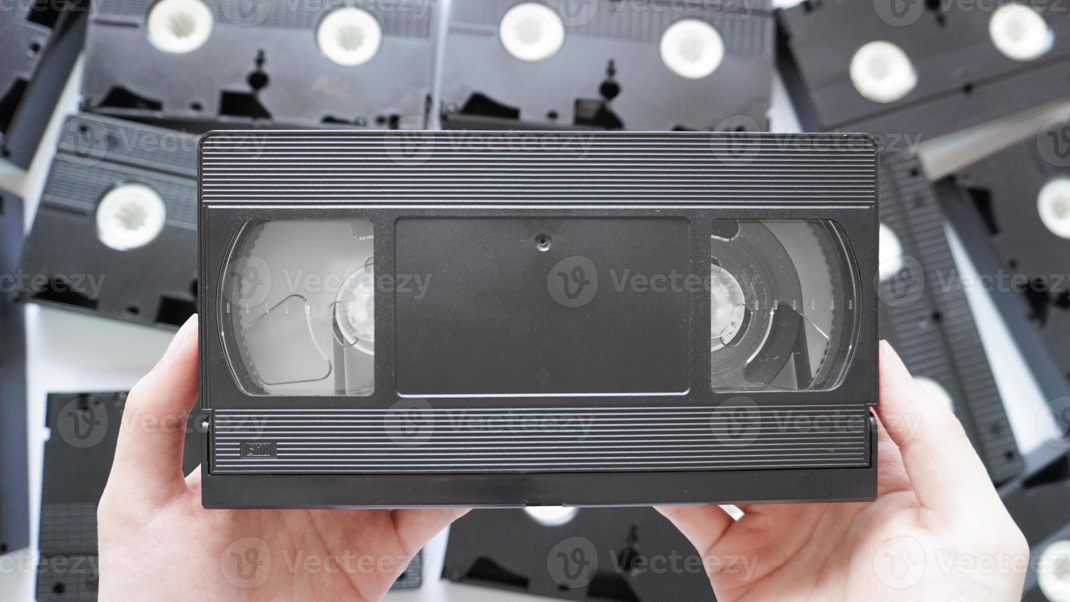 Hands holding a VHS tape back side with scattered tapes in the