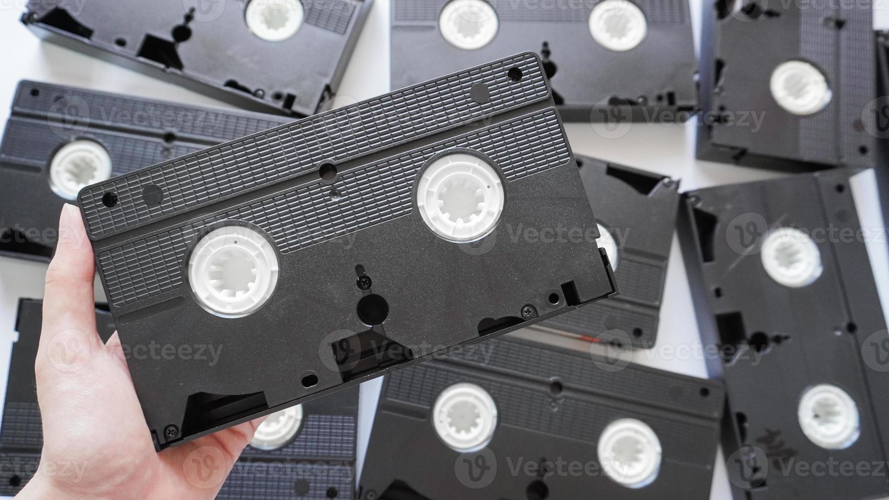 Hands holding a VHS tape back side with scattered tapes in the