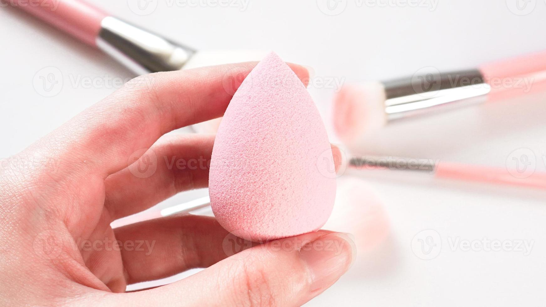 Woman's hand holding a clean makeup sponge with blurred make up brushes