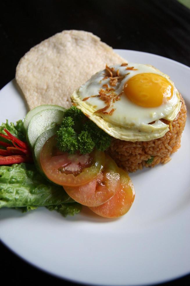 Nasi goreng fried rice with shrimps and egg garnished with fresh cucumber slices and prawn crackers on a white plate . Asian food. photo