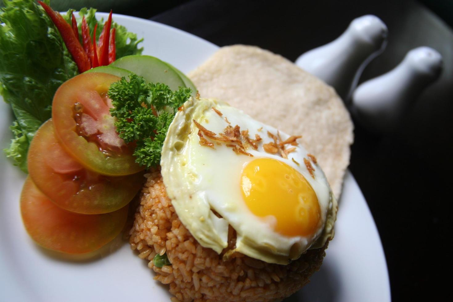 Nasi goreng fried rice with shrimps and egg garnished with fresh cucumber slices and prawn crackers on a white plate . Asian food. photo