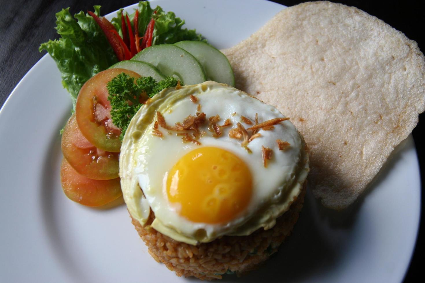 Nasi goreng fried rice with shrimps and egg garnished with fresh cucumber slices and prawn crackers on a white plate . Asian food. photo