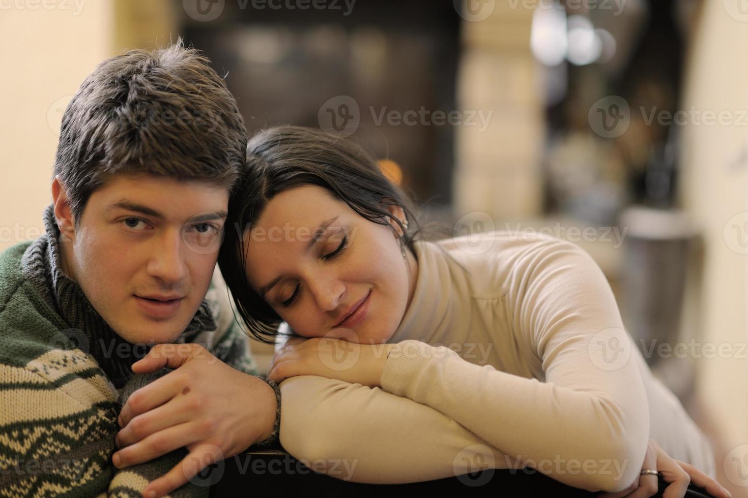 Young romantic couple sitting on sofa in front of fireplace at home photo