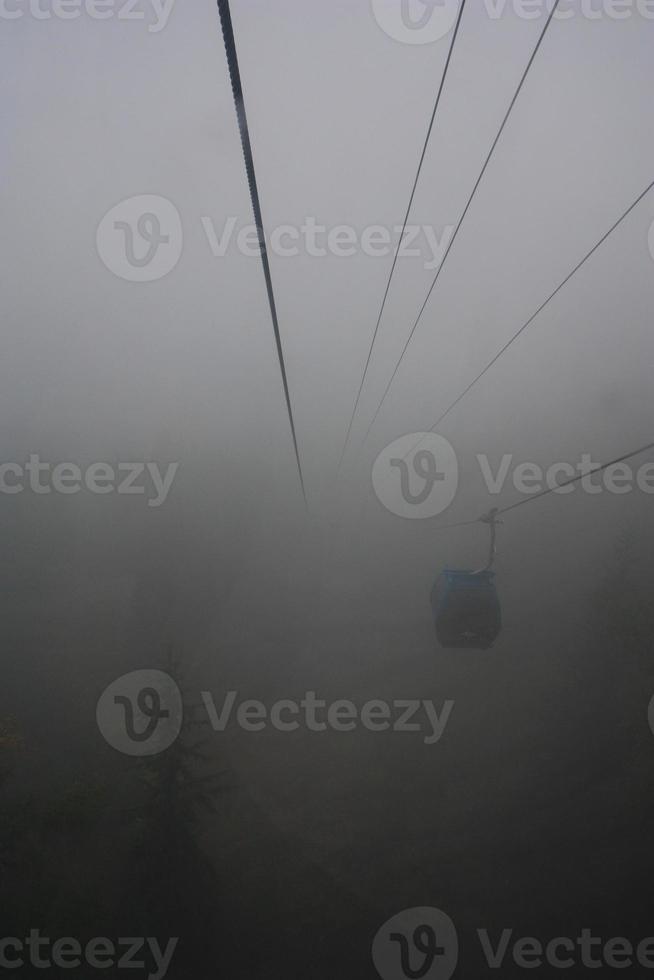A gondola going up a mountain through thick fog. photo
