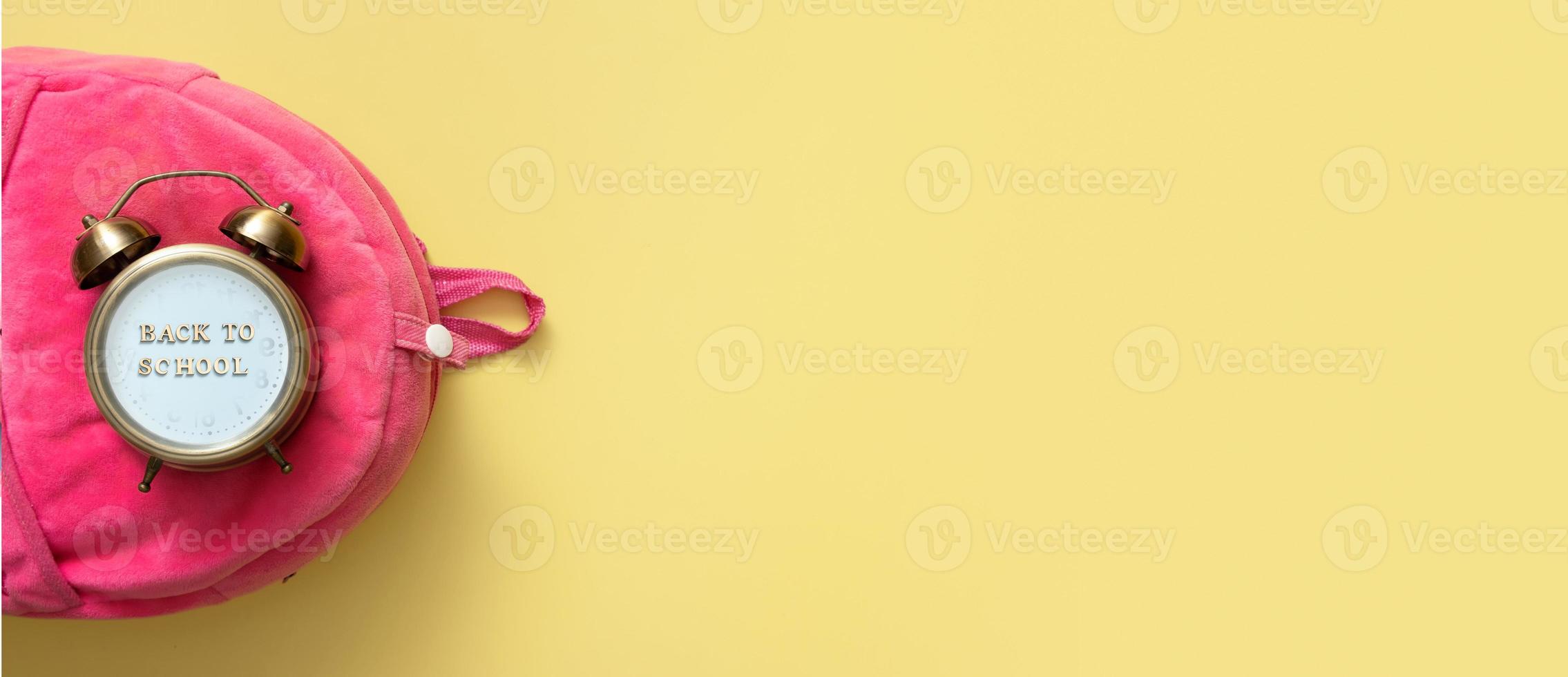 Alarm clock on pink backpack on colored background. Copy space. Back to school time concept photo