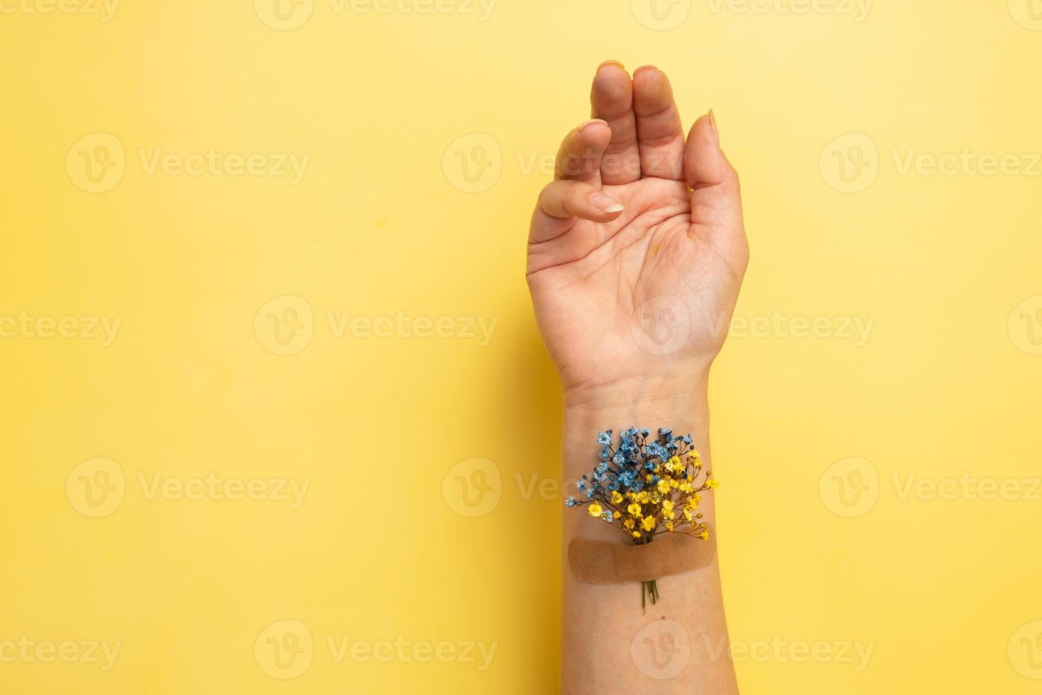 Blue and yellow flower under the patch on a female hand on yellow background. Treatment and recovery of Ukraine concept photo