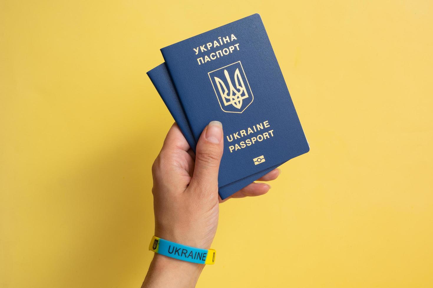 Passports of a citizen of Ukraine in a female hand on a yellow background, close-up. Inscription in Ukrainian Ukraine Passport photo