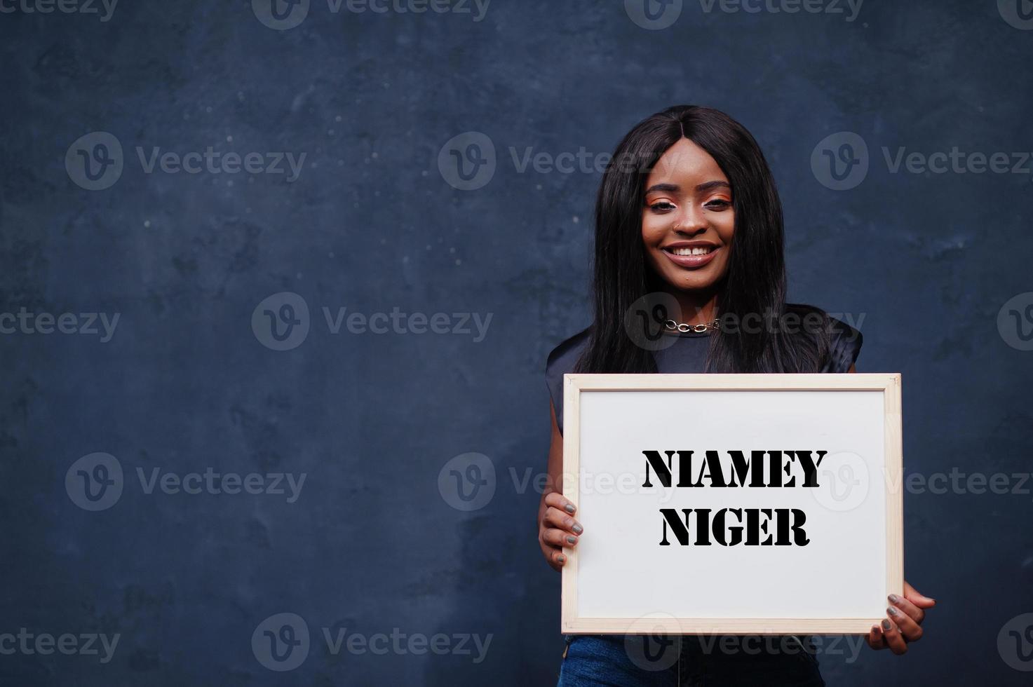 mujer africana sostiene una pizarra blanca con la inscripción niamey niger. concepto de ciudad más poblada de África. foto