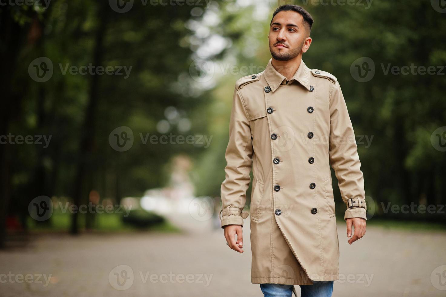 Stylish kuwaiti man at trench coat walking at park. photo