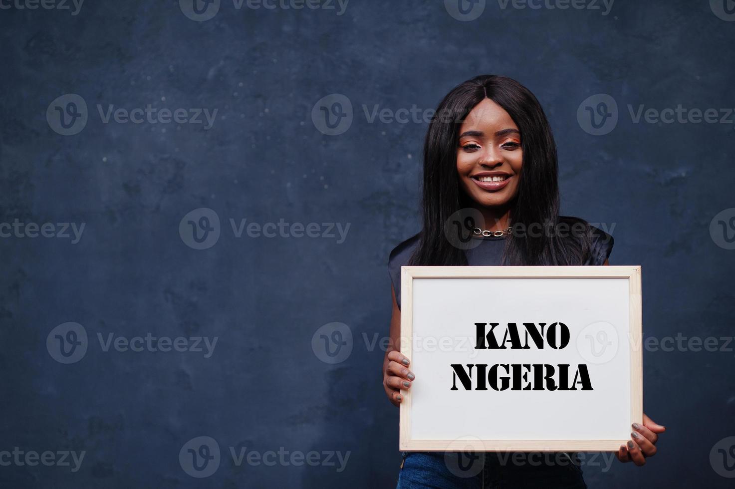 mujer africana sostiene una pizarra blanca con la inscripción kano nigeria. concepto de ciudad más poblada de África. foto