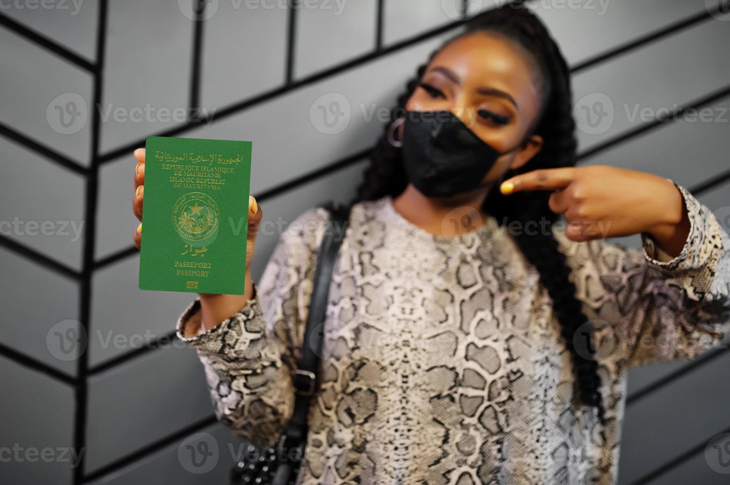 African woman wearing black face mask show Mauritania passport in hand. Coronavirus in Africa country, border closure and quarantine, virus outbreak concept. photo