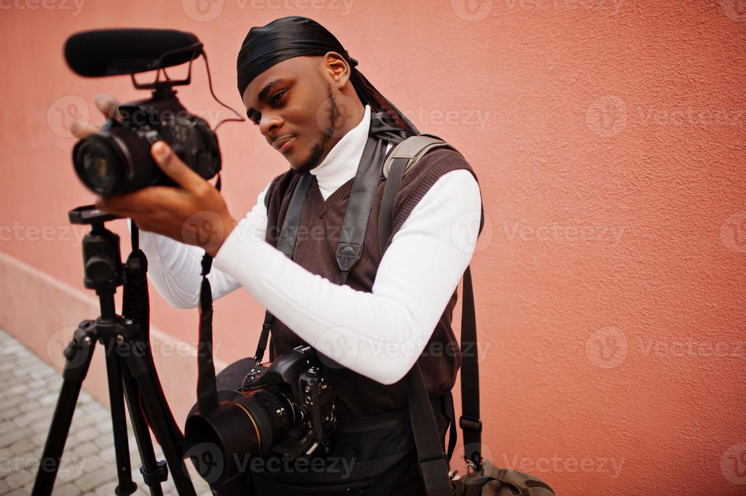 Young professional african american videographer holding professional camera with pro equipment. Afro cameraman wearing black duraq making a videos. photo