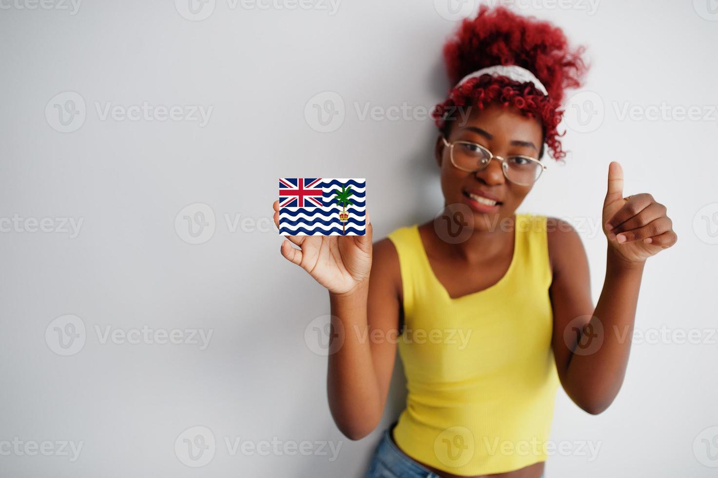 African woman with afro hair, wear yellow singlet and eyeglasses, hold British Indian Ocean Territory flag isolated on white background, show thumb up. photo