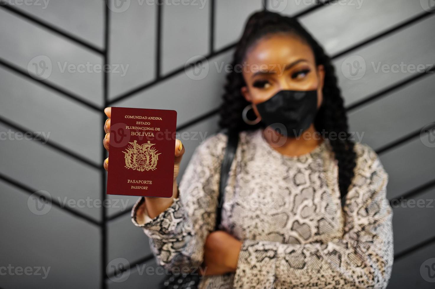 mujer afroamericana con mascarilla negra muestra el pasaporte boliviano en la mano. coronavirus en el país de América, cierre de fronteras y cuarentena, concepto de brote de virus. foto