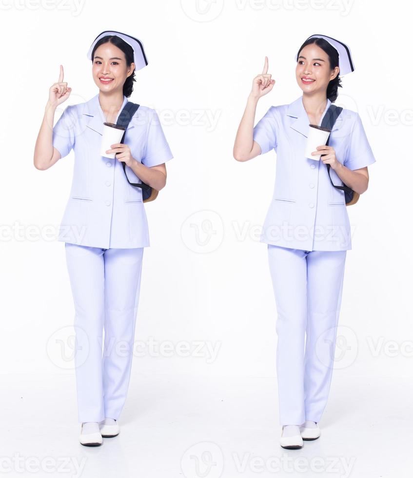 Full length 30s 20s Asian Woman Nurse hospital, pointing finger up in Air, wear formal uniform pant shoes. Smile Hospital female carry backpack coffee cup internet phone over white background isolated photo