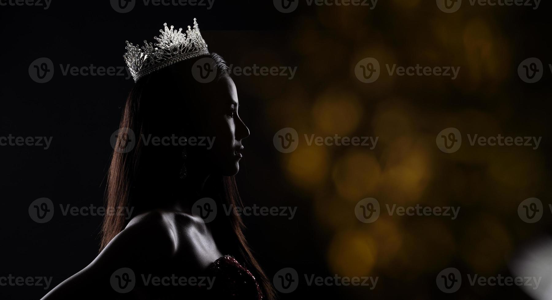 Portrait of Miss Pageant Beauty Contest in sequin Evening Ball Gown long dress with sparkle light Diamond Crown, silhouette low key exposure with curtain, studio lighting dark background dramatic photo