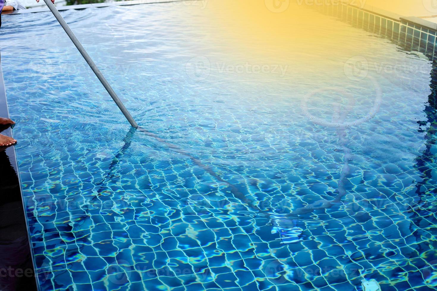 Woman Worker clean private swimming pool with vacuum blue tube cleaner every week in Summer, Salt type Pool along with Ocean as horizontal style with coconut trees photo