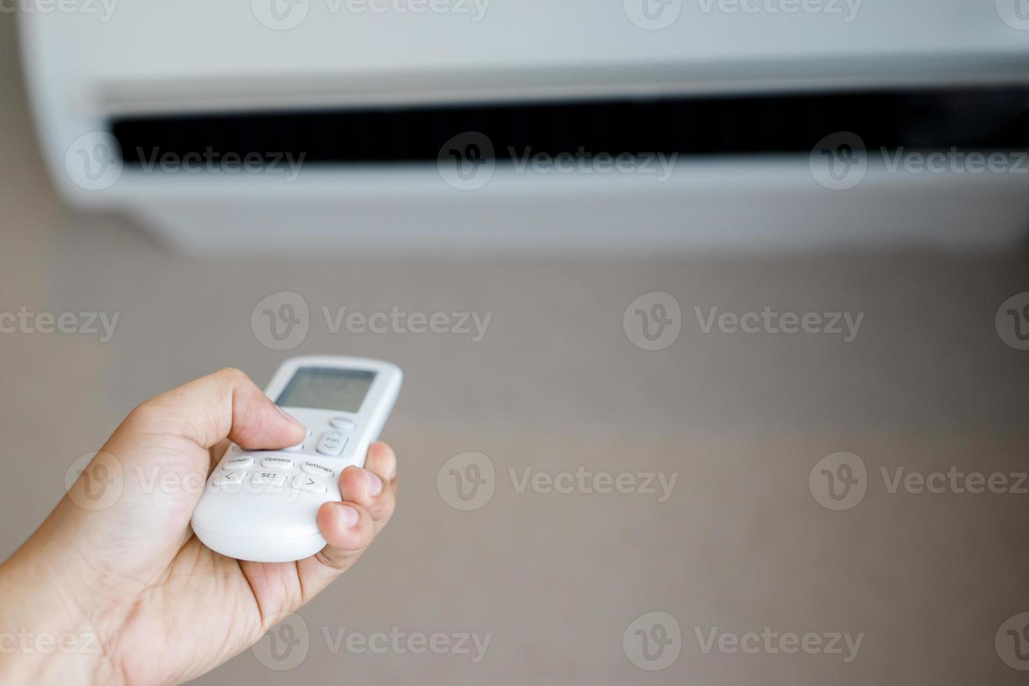 Air conditioner inside the room with close up man hand holding using directed operating remote controller. photo