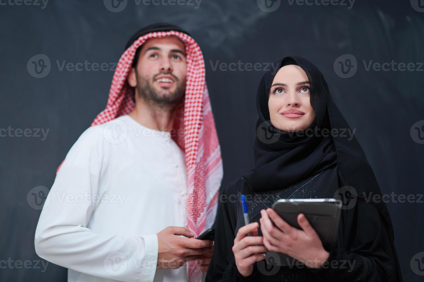 muslim couple using modern technology in front of black chalkboard photo