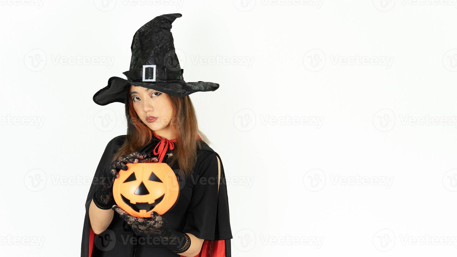 Asian cute beautiful girl with black and orange hair in halloween make up posing with pumpkin and looking at the camera over white background photo