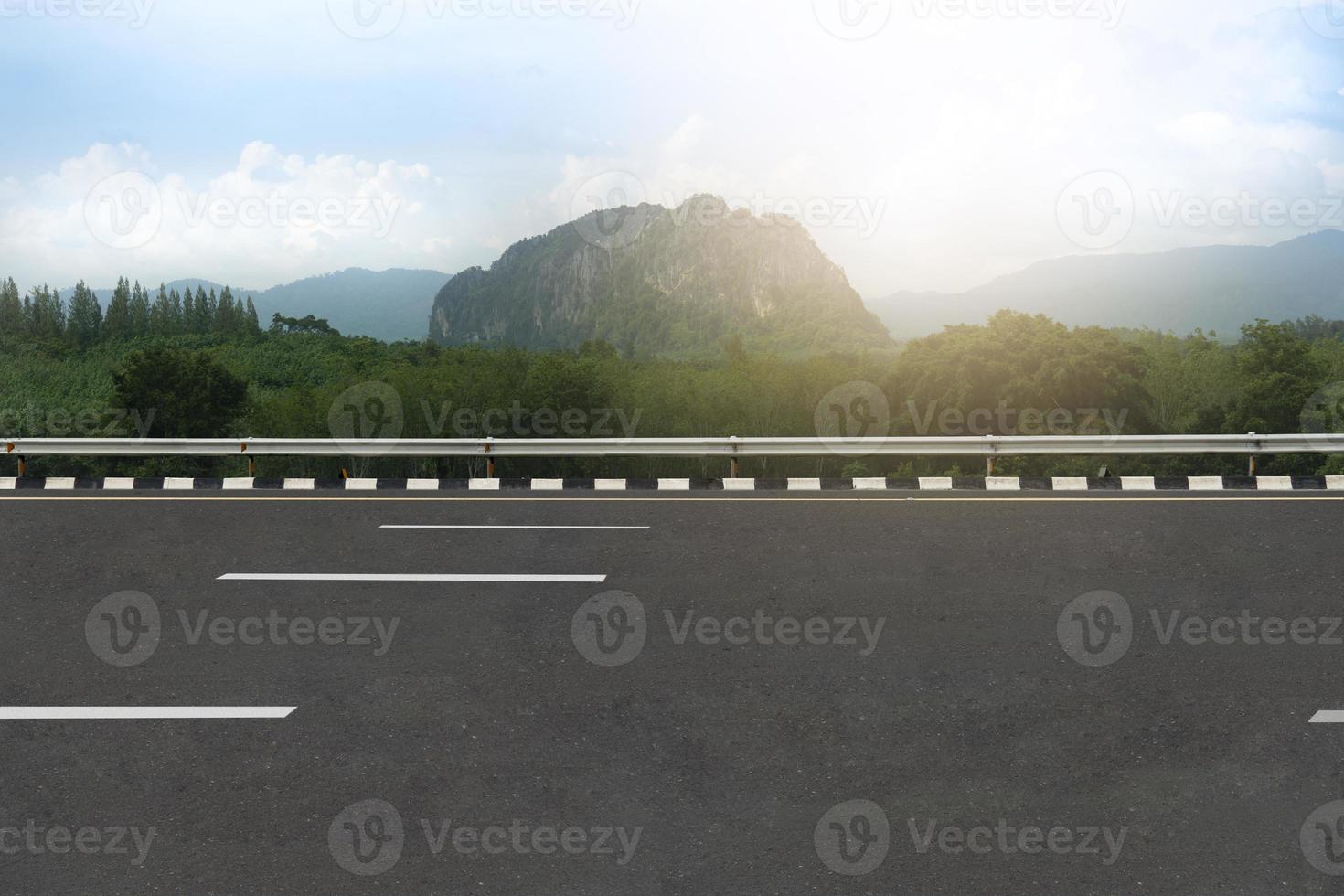 vista horizontal del vacío borroso de la carretera asfaltada con la carretera. fondo de bosque verde y montañas bajo el cielo azul con nubes blancas. foto