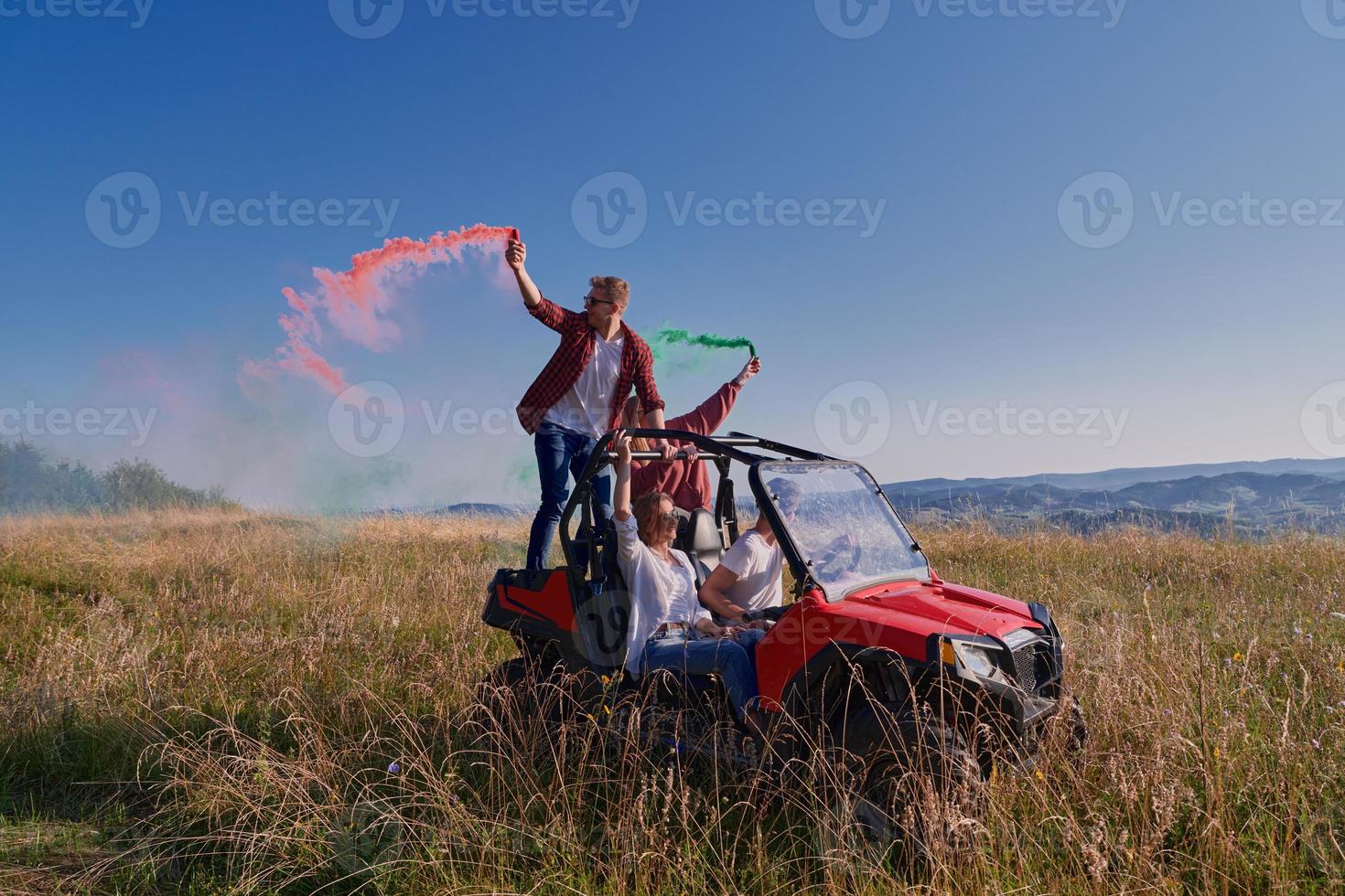 gente emocionada divirtiéndose disfrutando de un hermoso día soleado sosteniendo antorchas coloridas mientras conduce un coche de buggy fuera de la carretera foto