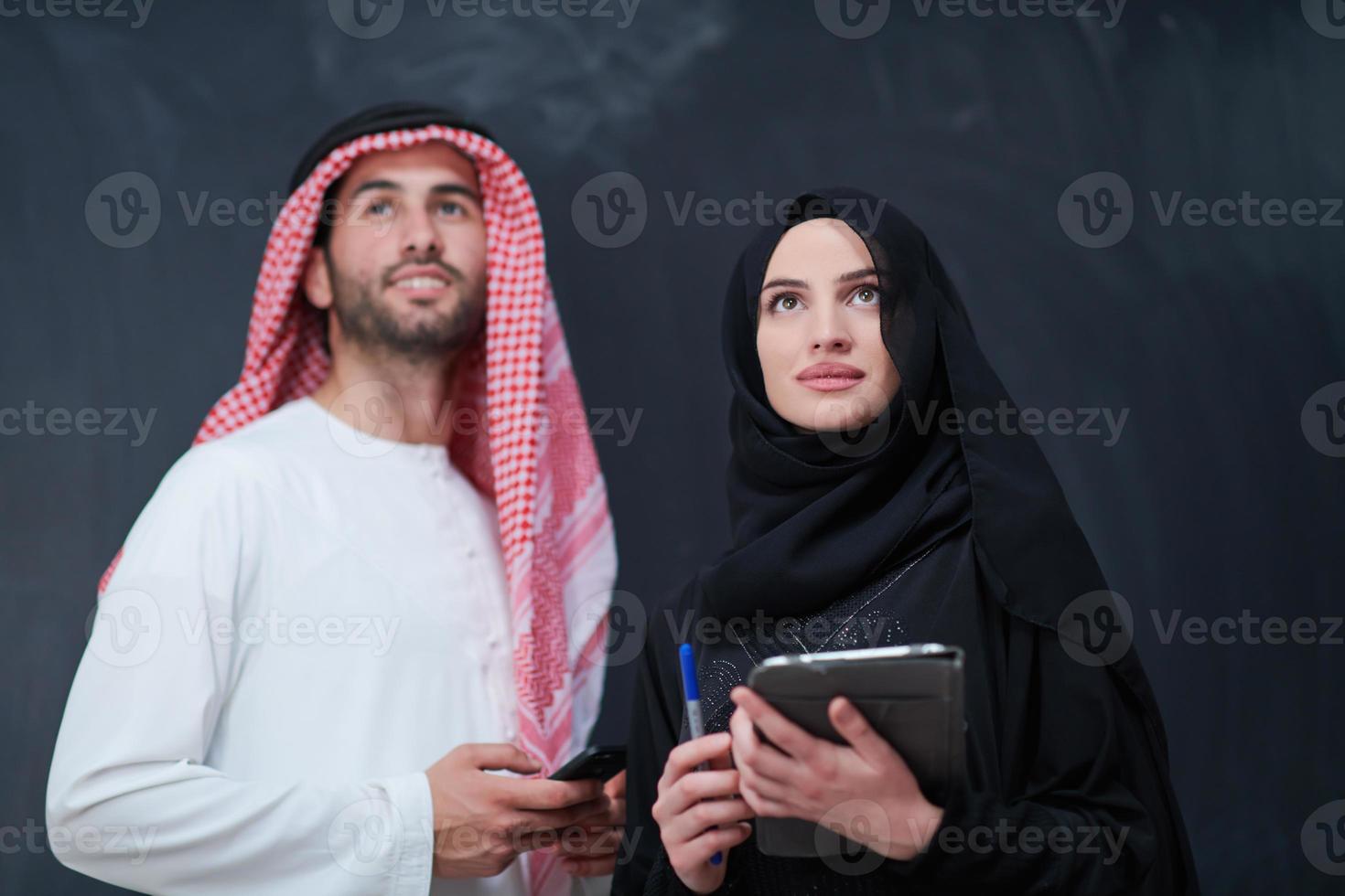 muslim couple using modern technology in front of black chalkboard photo