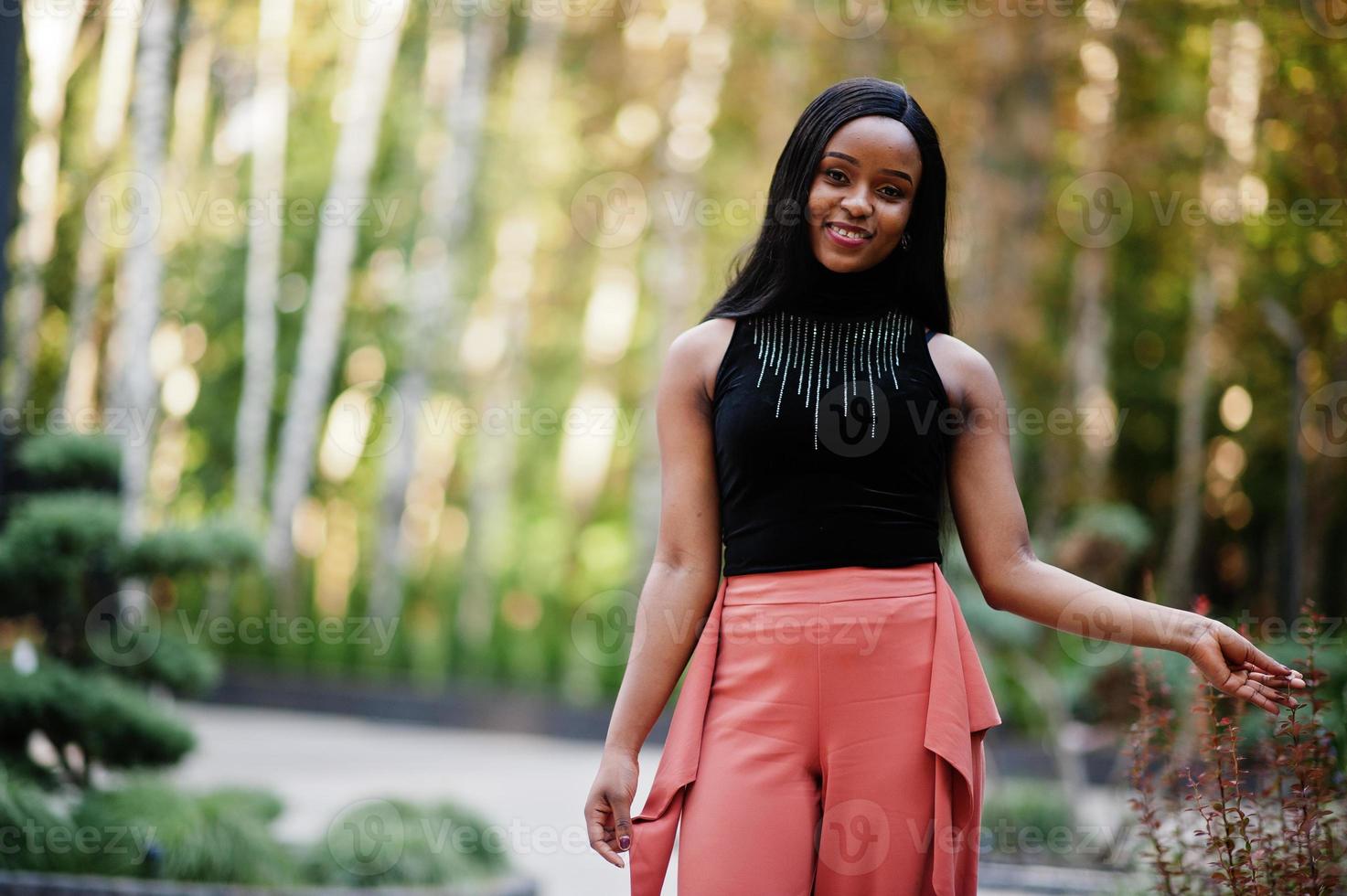 Fashionable african american woman in peach pants and black blouse pose outdoor. photo