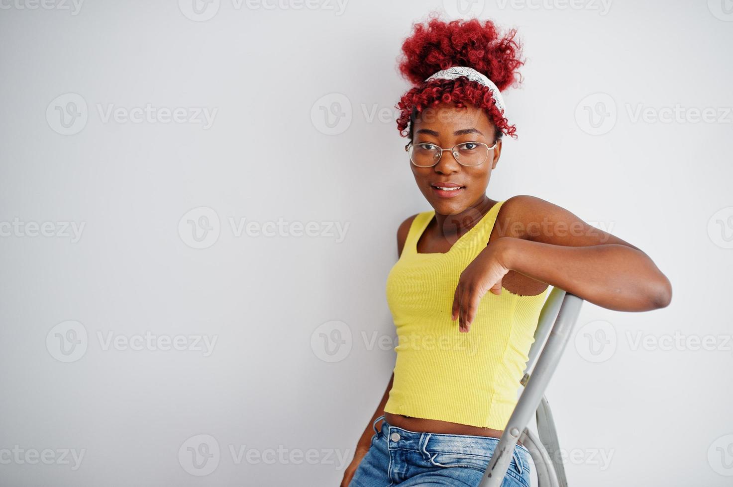 African american woman in yellow singlet and eyglasses against white wall stand om iron ladder. photo