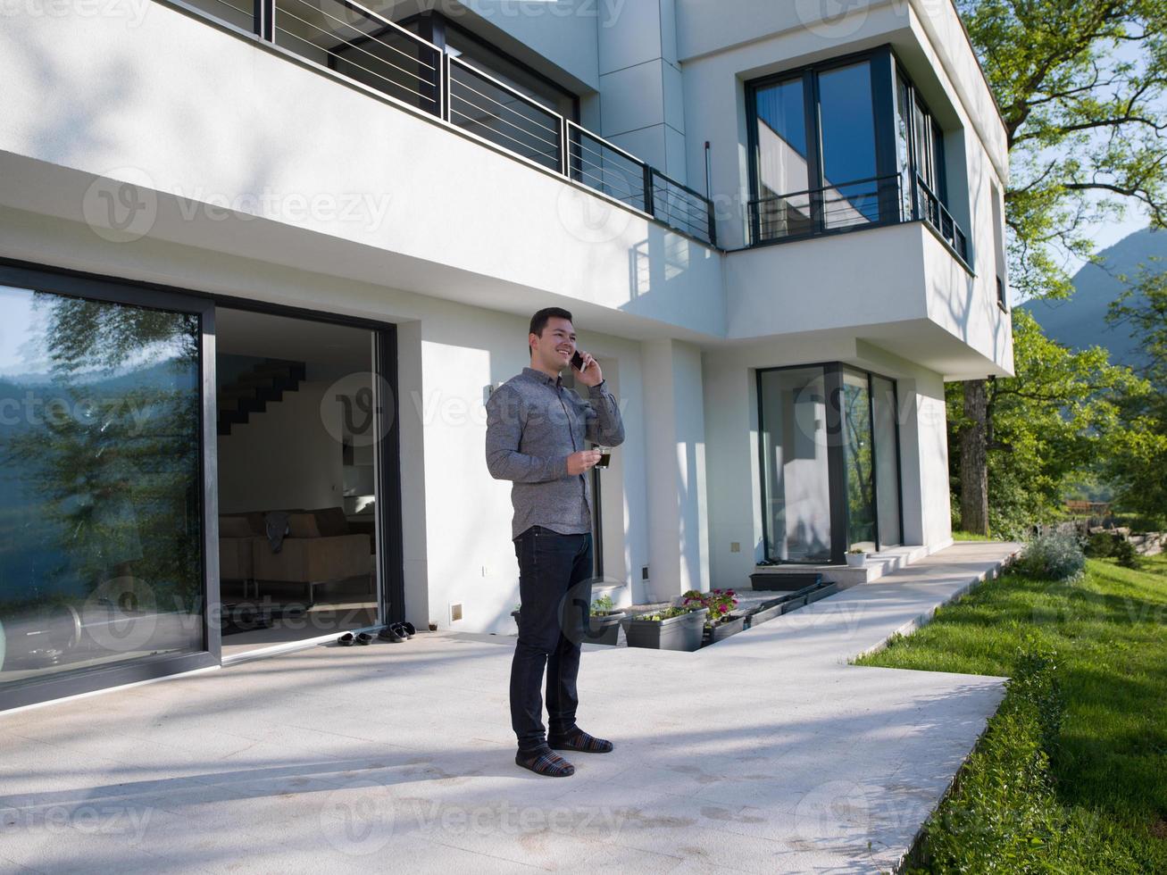 man using mobile phone in front of his luxury home villa photo