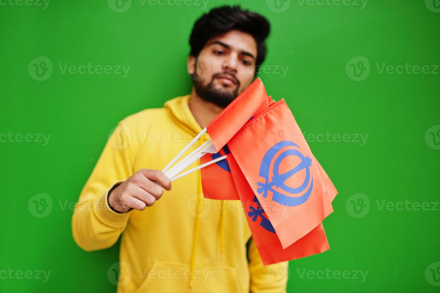 Happy Guru Nanak Jayanti concept. Young indian man in yellow sweatshirt hold flags. Cool south asian guy wear hoodie celebrating India holiday. photo