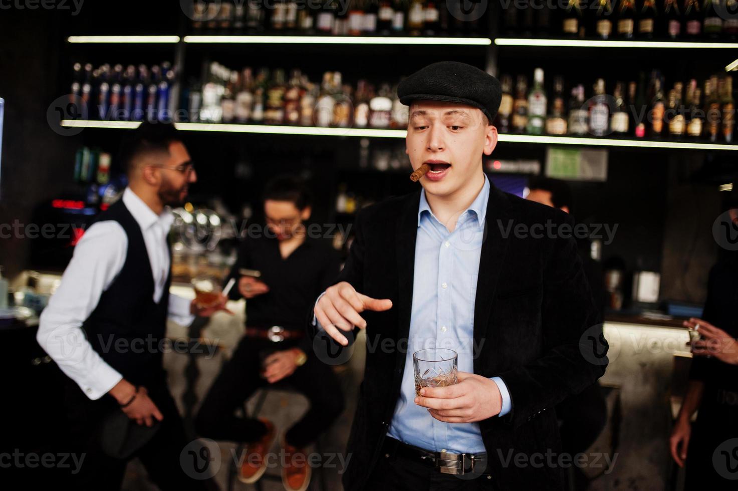Stylish arab man against group of handsome retro well-dressed guys gangsters spend time at club, drinking on bar counter. Multiethnic male bachelor mafia party in restaurant. photo
