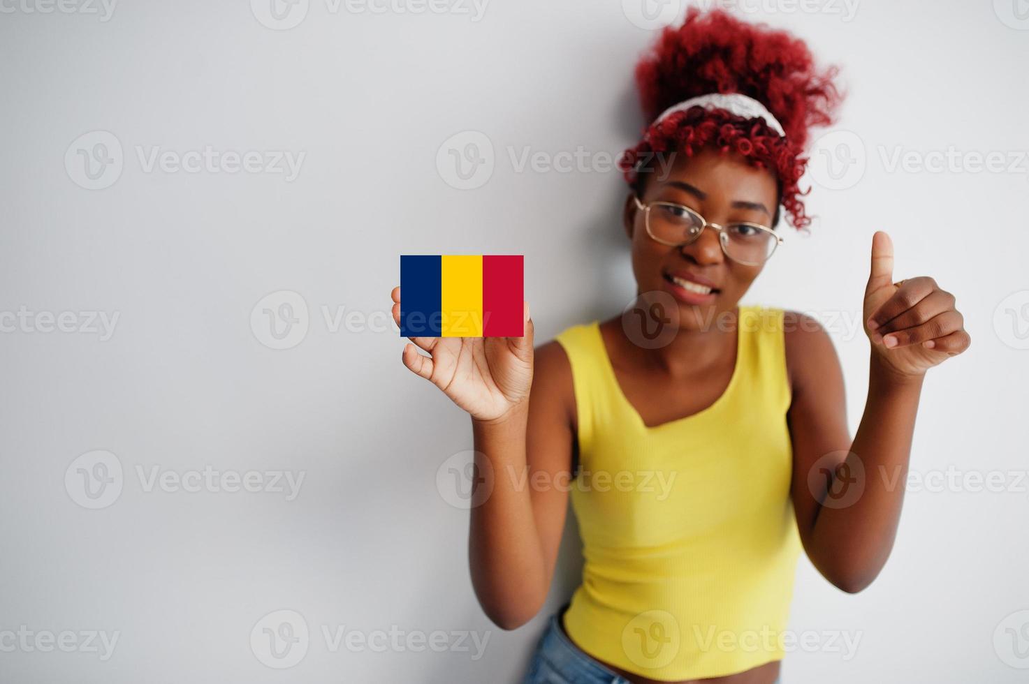 African woman with afro hair, wear yellow singlet and eyeglasses, hold Chad flag isolated on white background, show thumb up. photo