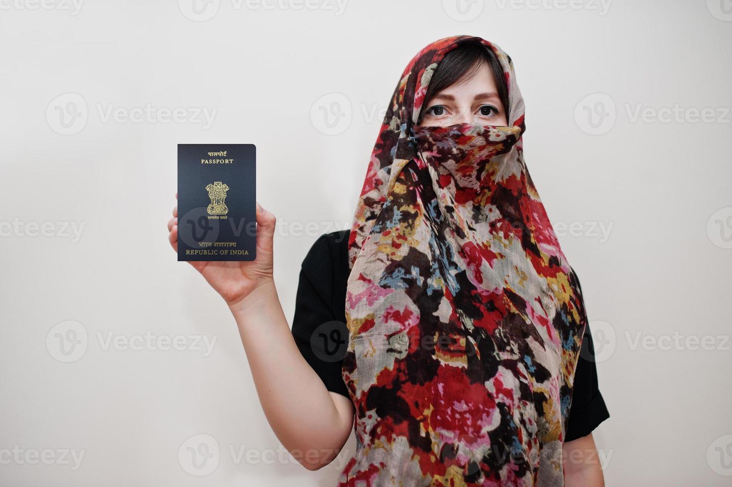 Young arabian muslim woman in hijab clothes hold Republic of India passport on white wall background, studio portrait. photo