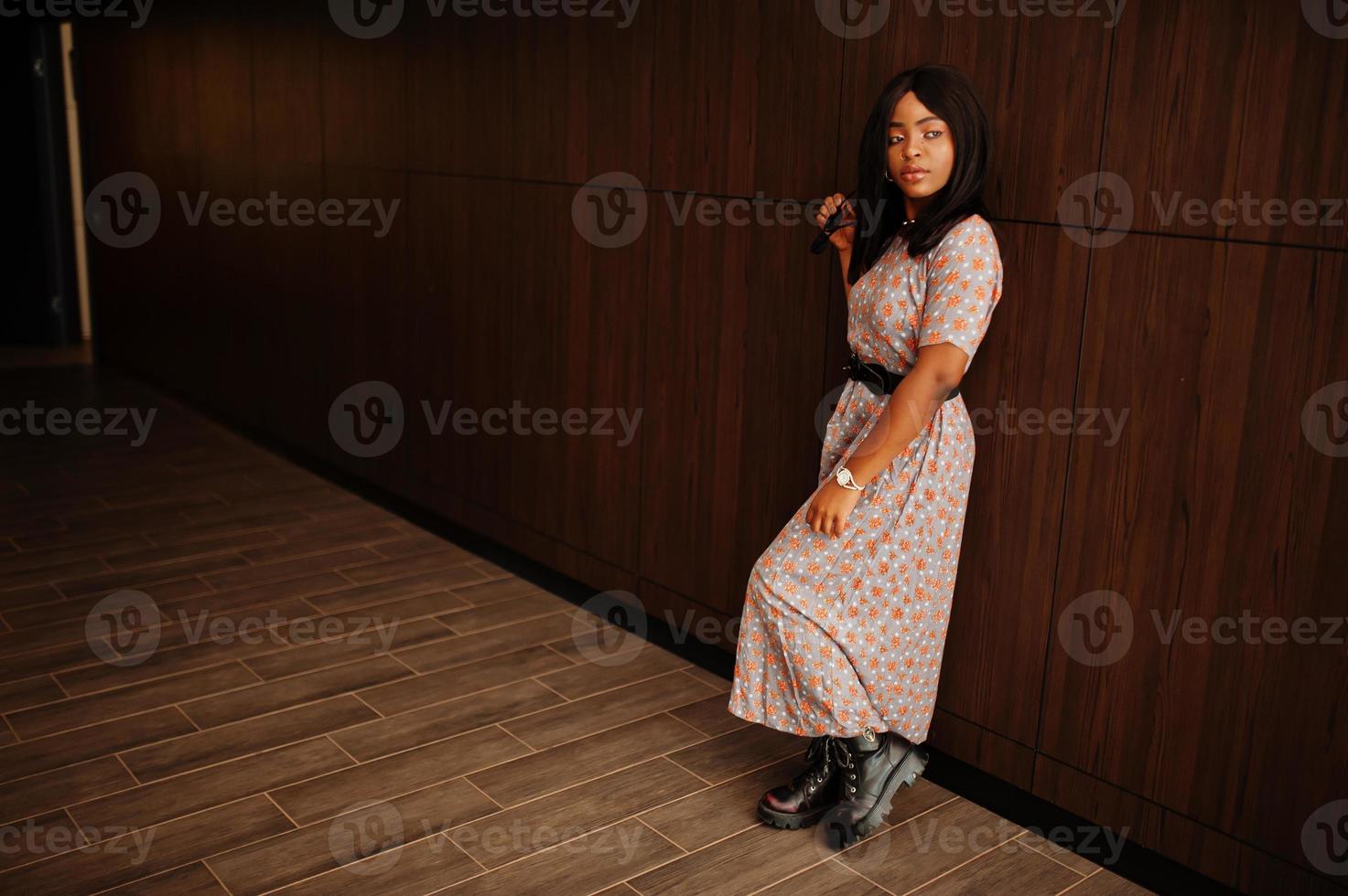 Fashion portrait of african american woman in long dress, boots and sunglasses indoor. photo
