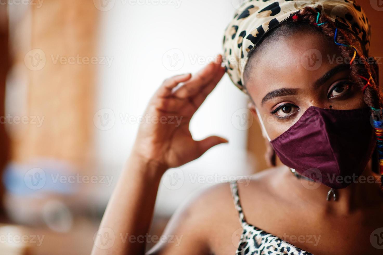 Stylish african american woman with dreadlocks afro hair, wear face protect  mask and headdress leopard scarf at restaurant. New normal life after coronavirus epidemic. photo