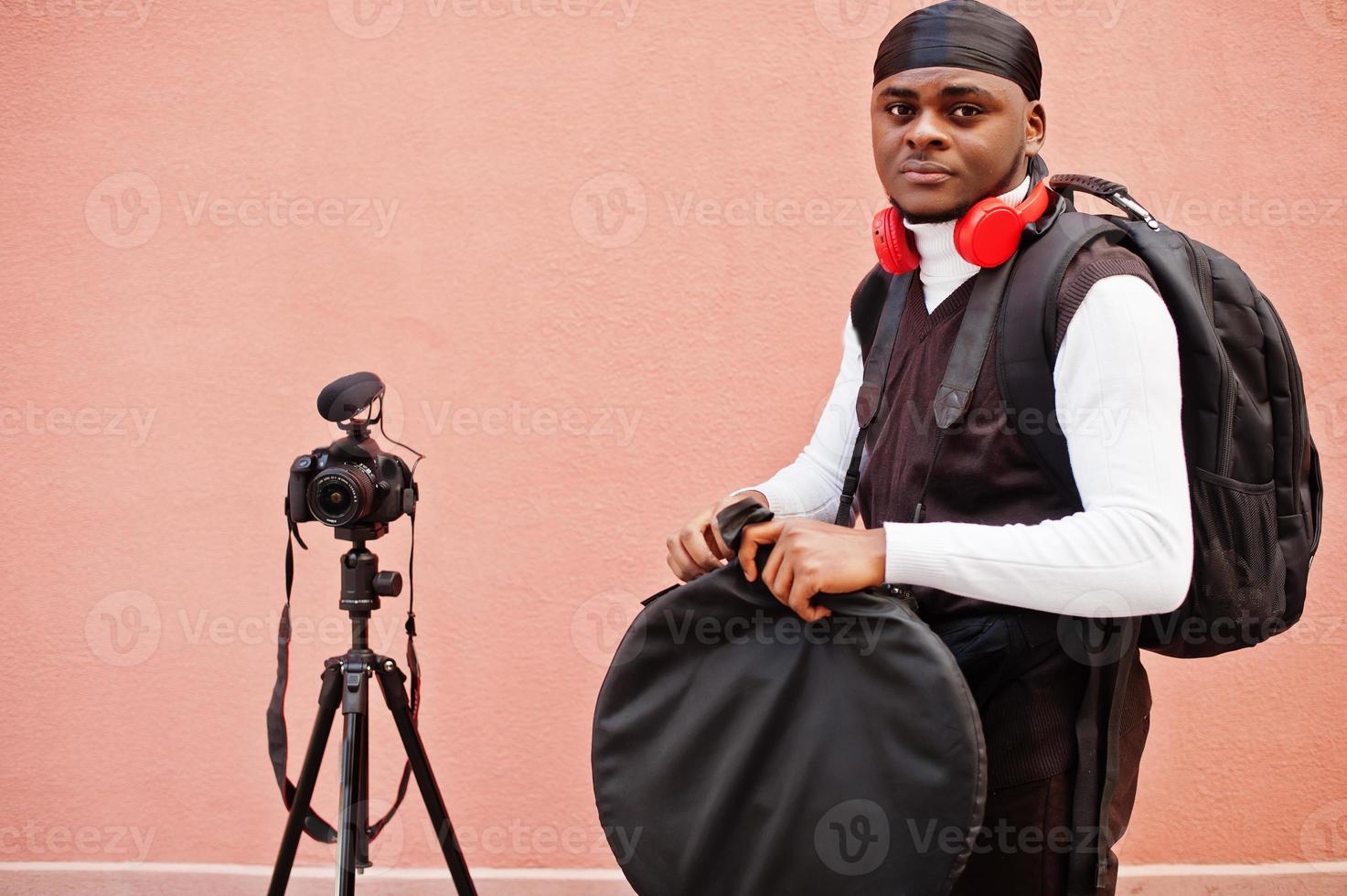 Young professional african american videographer holding professional camera with pro equipment. Afro cameraman wearing black duraq making a videos. photo