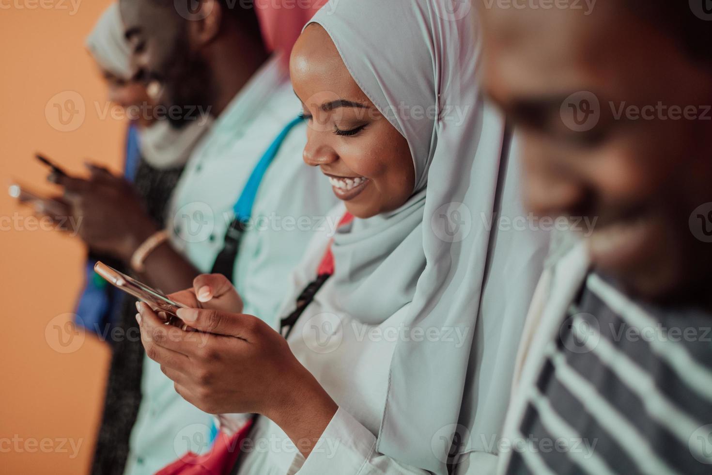 A group of African Muslim students use smartphones while standing in front of a yellow background photo