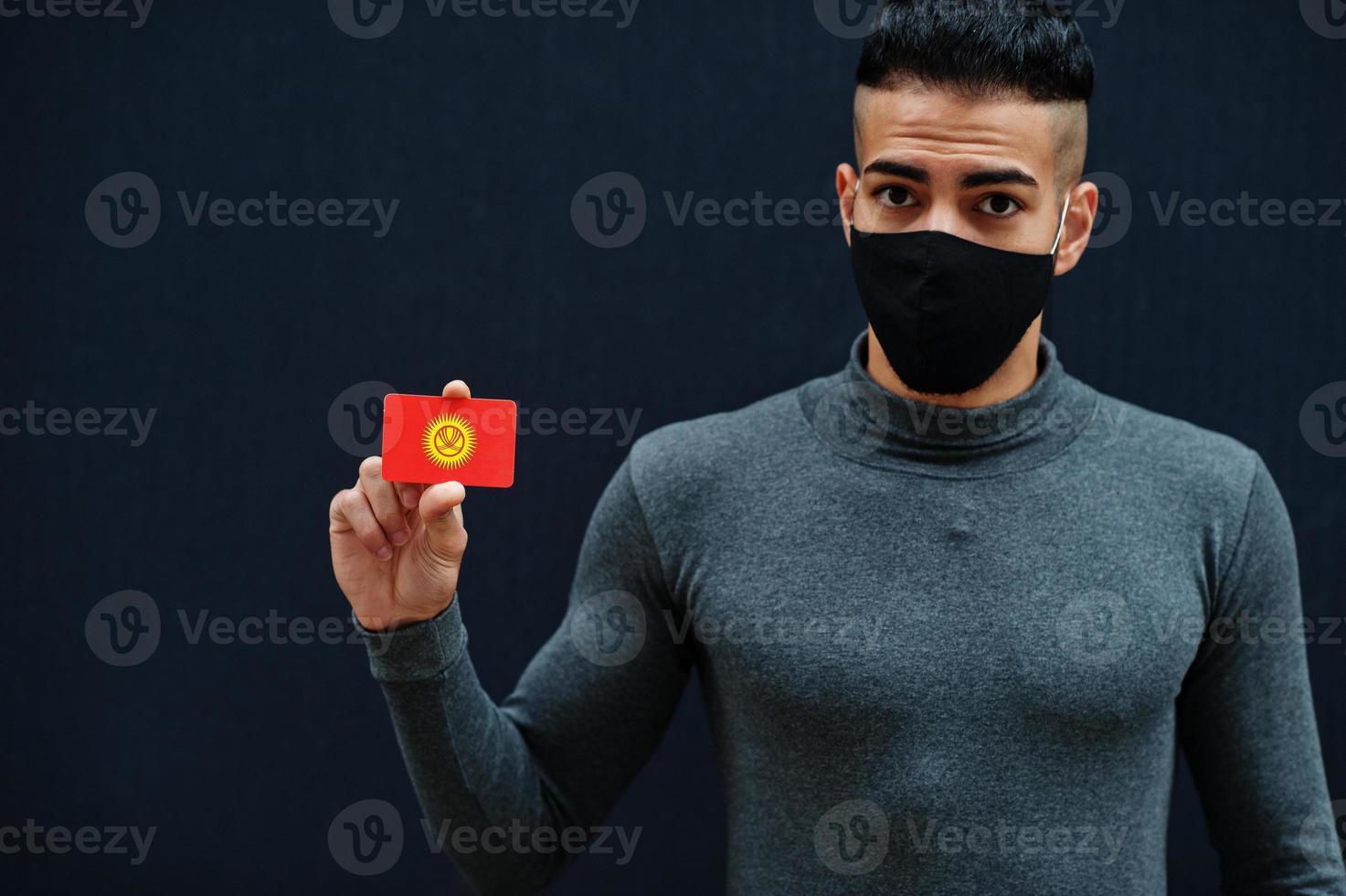 Middle eastern man in gray turtleneck and black face protect mask show Kyrgyzstan flag isolated background. photo