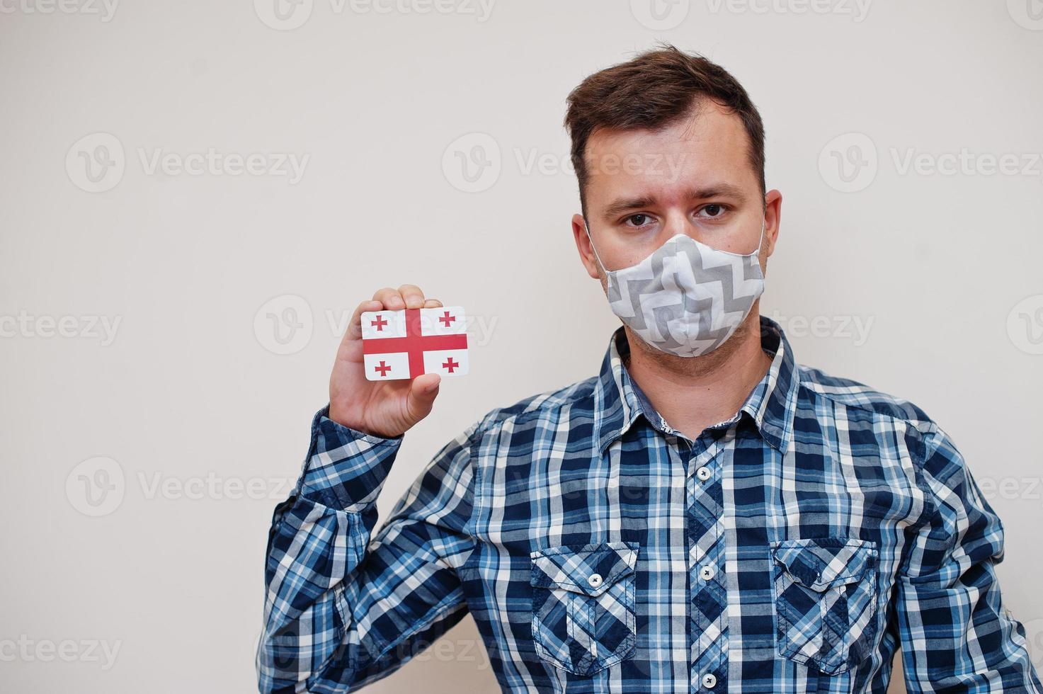 Man in checkered shirt show Georgia flag card in hand, wear protect mask isolated on white background. Asian countries Coronavirus concept. photo