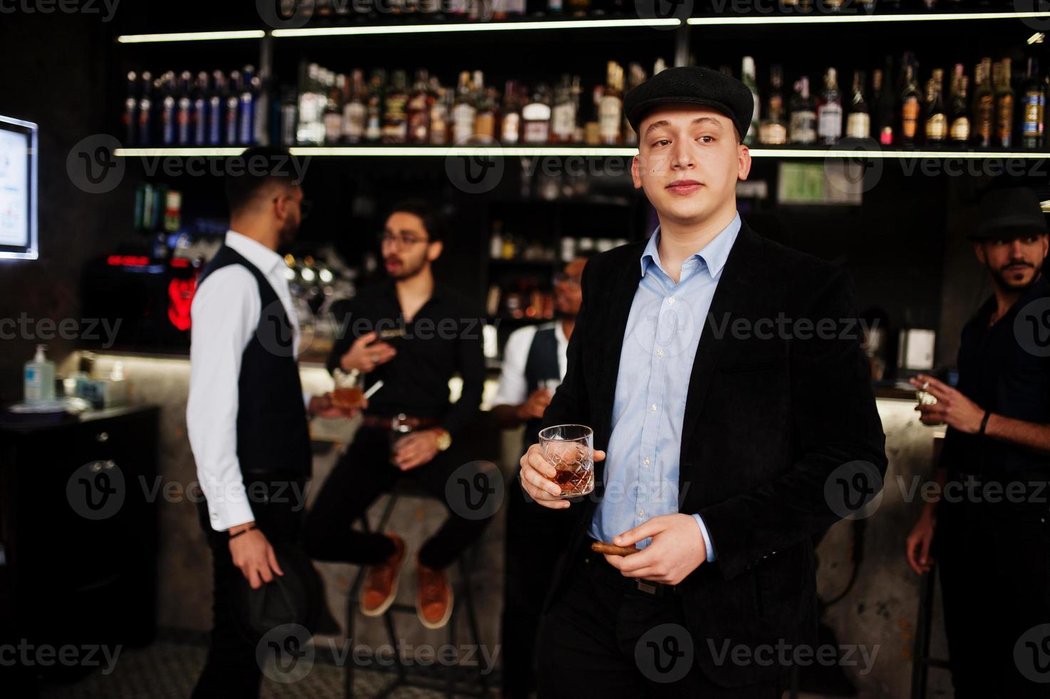 Stylish arab man against group of handsome retro well-dressed guys gangsters spend time at club, drinking on bar counter. Multiethnic male bachelor mafia party in restaurant. photo