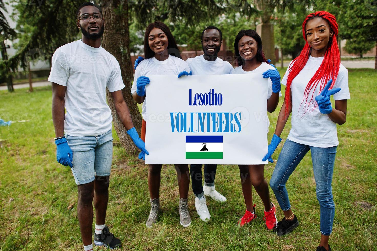 Group of happy african volunteers hold blank with Lesotho flag in park. Africa countries volunteering, charity, people and ecology concept. photo