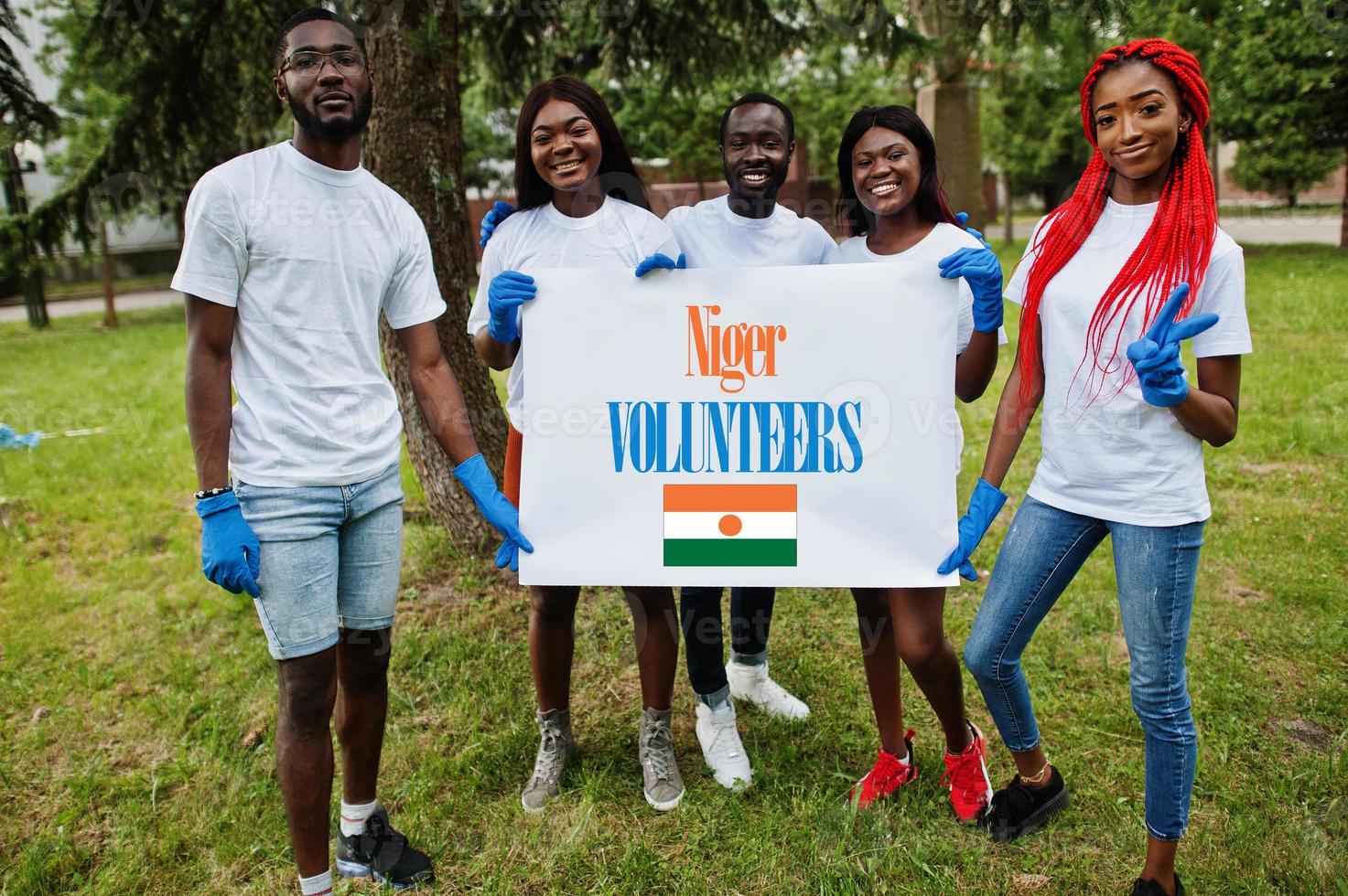 Group of happy african volunteers hold blank with Niger flag in park. Africa countries volunteering, charity, people and ecology concept. photo