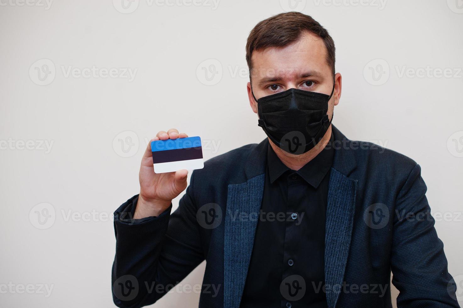 European man wear black formal and protect face mask, hold Estonia flag card isolated on white background. Europe coronavirus Covid country concept. photo