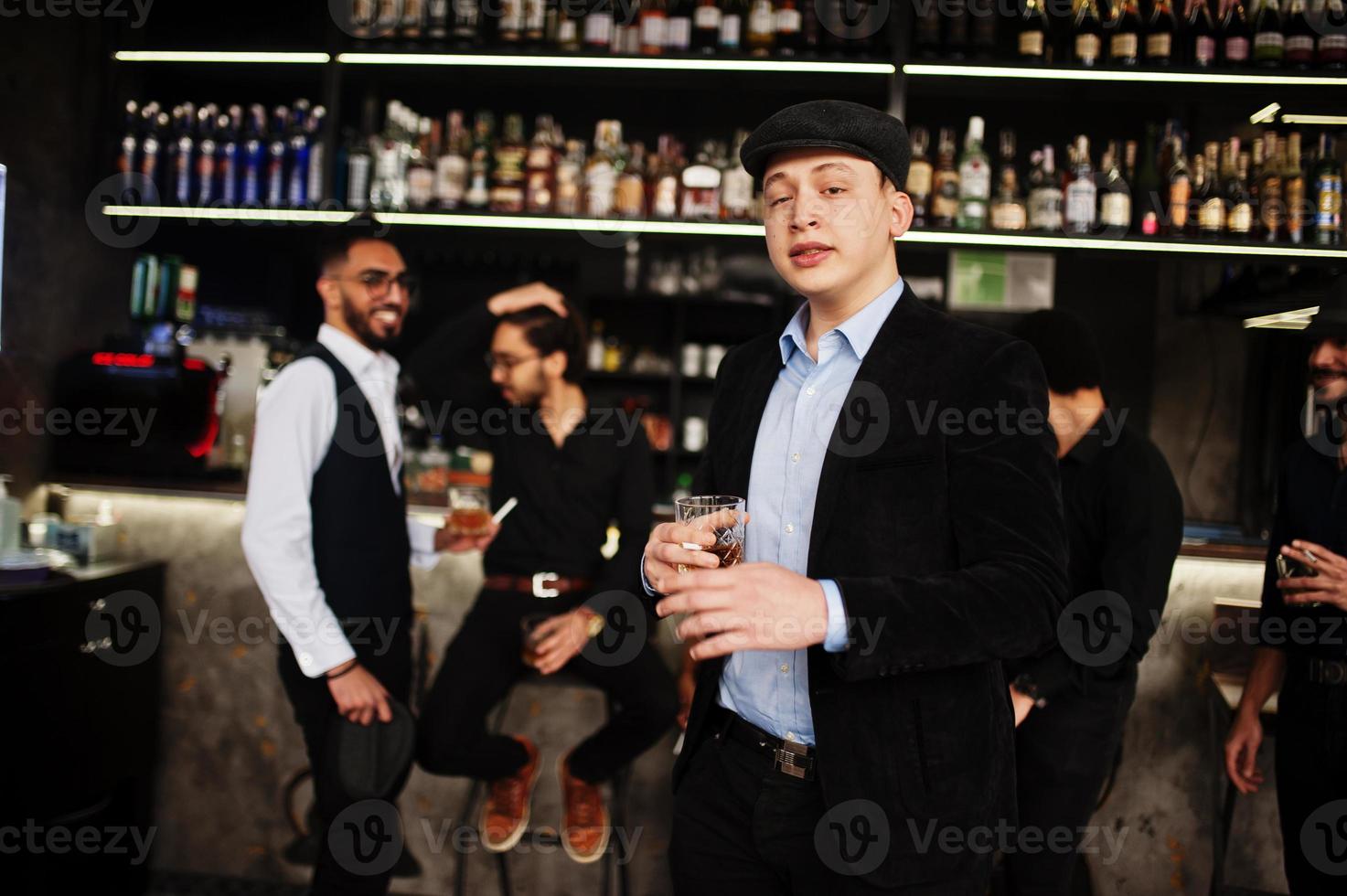Stylish arab man against group of handsome retro well-dressed guys gangsters spend time at club, drinking on bar counter. Multiethnic male bachelor mafia party in restaurant. photo